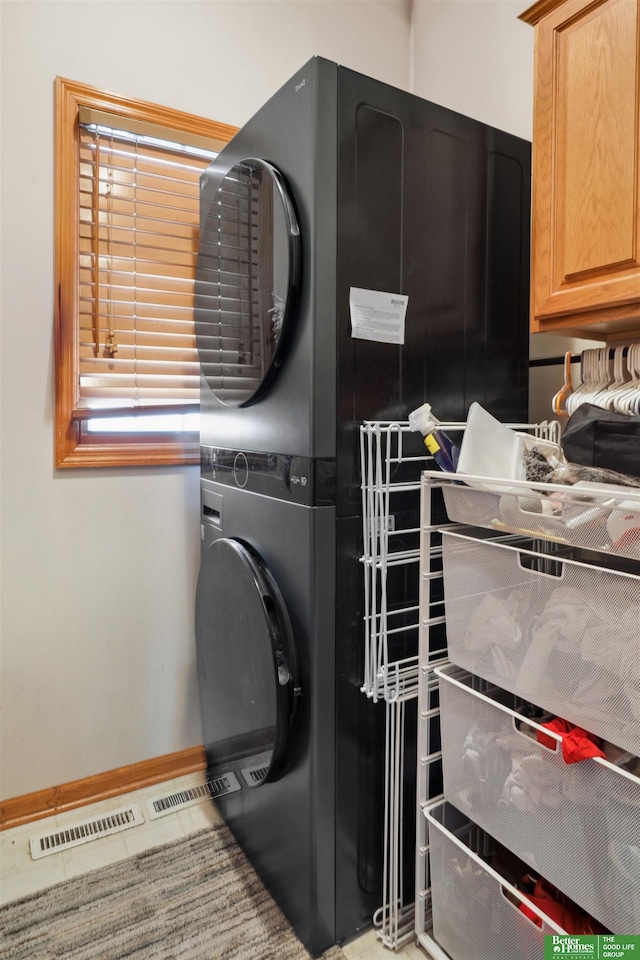 washroom featuring cabinet space, stacked washing maching and dryer, visible vents, and baseboards