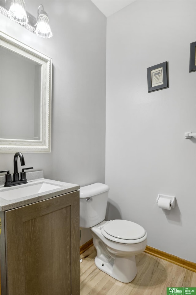 half bath featuring toilet, vanity, wood finished floors, and baseboards