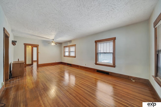unfurnished room featuring a textured ceiling, hardwood / wood-style flooring, ceiling fan, baseboards, and visible vents