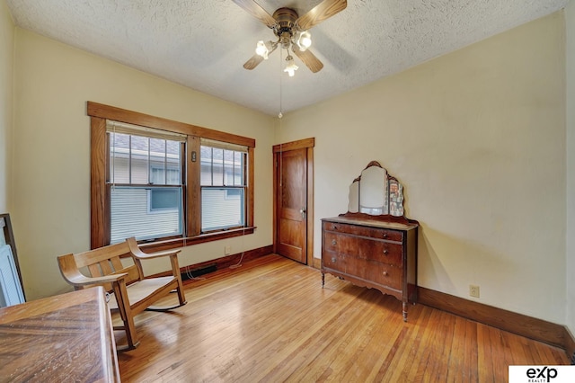 living area featuring a ceiling fan, baseboards, a textured ceiling, and light wood-style flooring