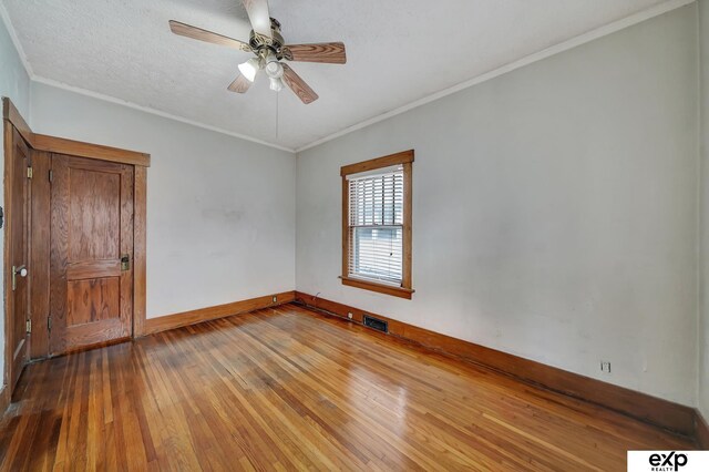 spare room featuring visible vents, ornamental molding, baseboards, hardwood / wood-style flooring, and ceiling fan