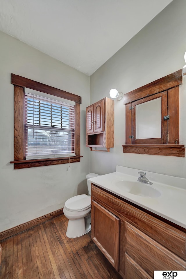 half bath featuring baseboards, toilet, vanity, and hardwood / wood-style floors
