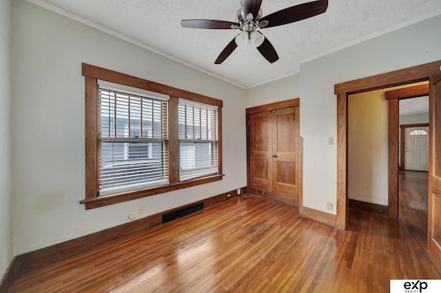 unfurnished bedroom featuring crown molding, hardwood / wood-style floors, a textured ceiling, baseboards, and visible vents
