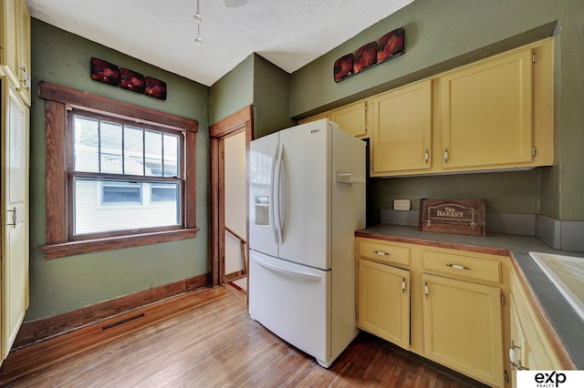 kitchen with white refrigerator with ice dispenser, light wood-style floors, and cream cabinetry