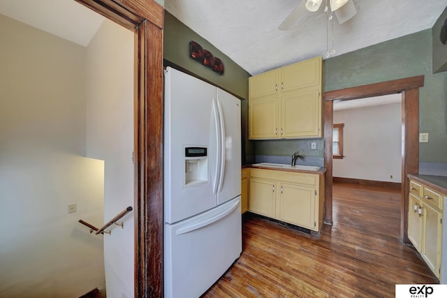 kitchen featuring white fridge with ice dispenser, wood finished floors, cream cabinetry, and a sink