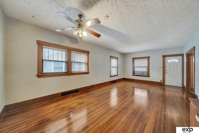 empty room with hardwood / wood-style floors, visible vents, a ceiling fan, baseboards, and a textured ceiling