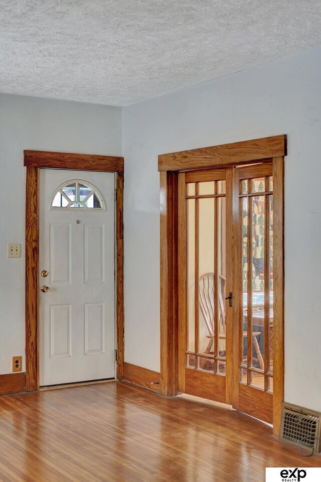 foyer entrance featuring baseboards, wood finished floors, visible vents, and a textured ceiling