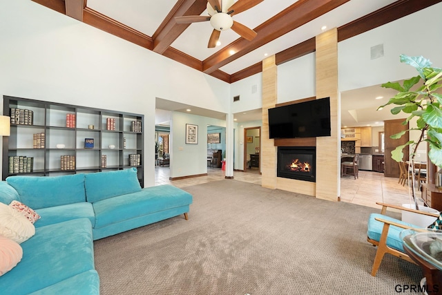 living area featuring ceiling fan, a high ceiling, beam ceiling, and a large fireplace