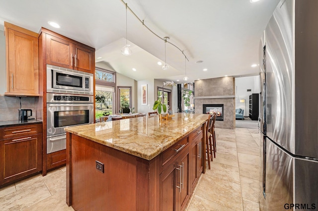 kitchen featuring stainless steel appliances, vaulted ceiling, a kitchen island, light stone countertops, and open floor plan
