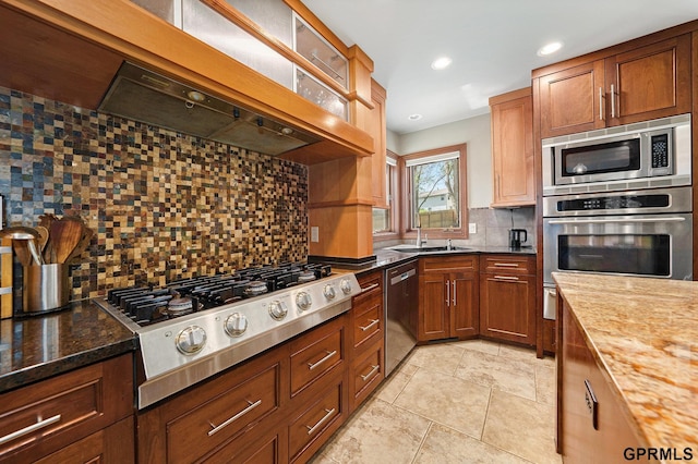 kitchen featuring exhaust hood, dark stone countertops, stainless steel appliances, a sink, and decorative backsplash