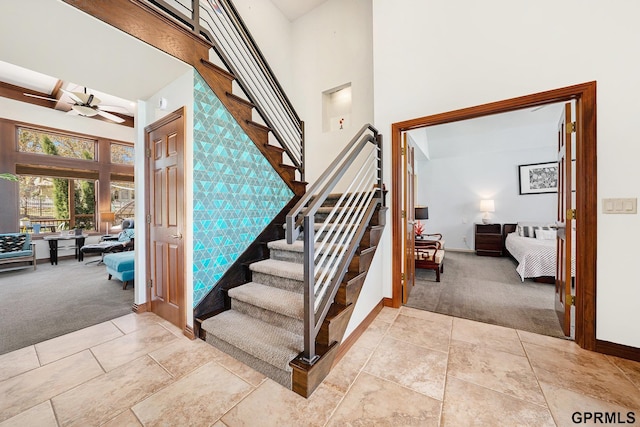 stairway featuring baseboards, a ceiling fan, a high ceiling, and carpet
