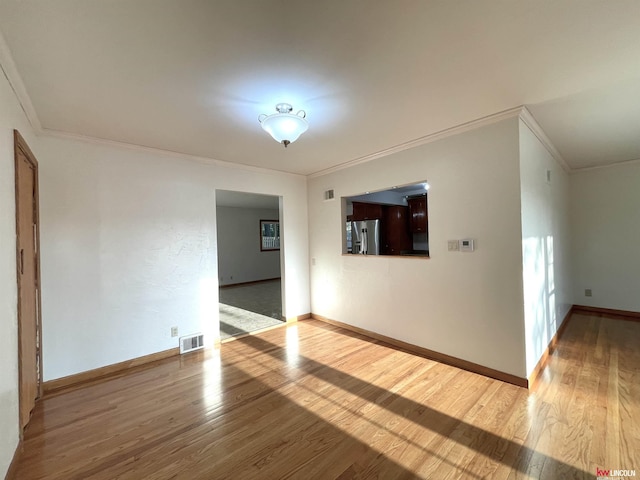 spare room featuring visible vents, baseboards, wood finished floors, and ornamental molding