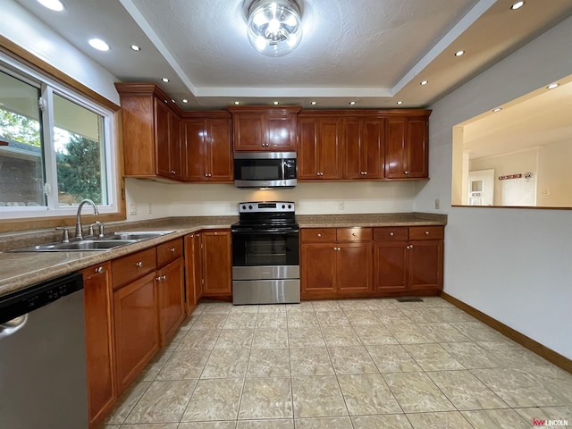 kitchen featuring a raised ceiling, brown cabinetry, stainless steel appliances, and a sink