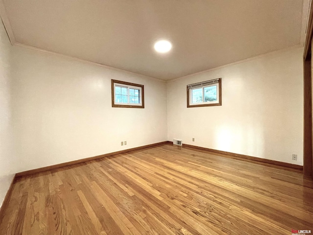 empty room with a healthy amount of sunlight, light wood finished floors, ornamental molding, and visible vents