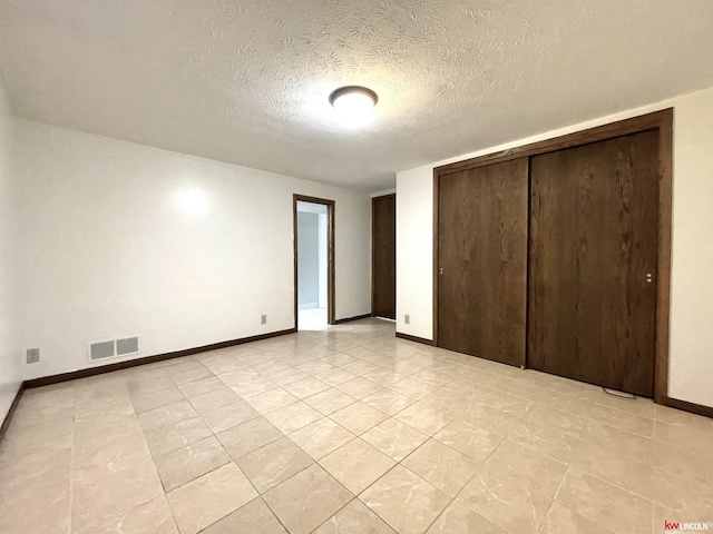 unfurnished bedroom with a textured ceiling, baseboards, visible vents, a closet, and light tile patterned floors