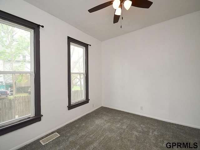 unfurnished room with dark carpet, visible vents, ceiling fan, and baseboards