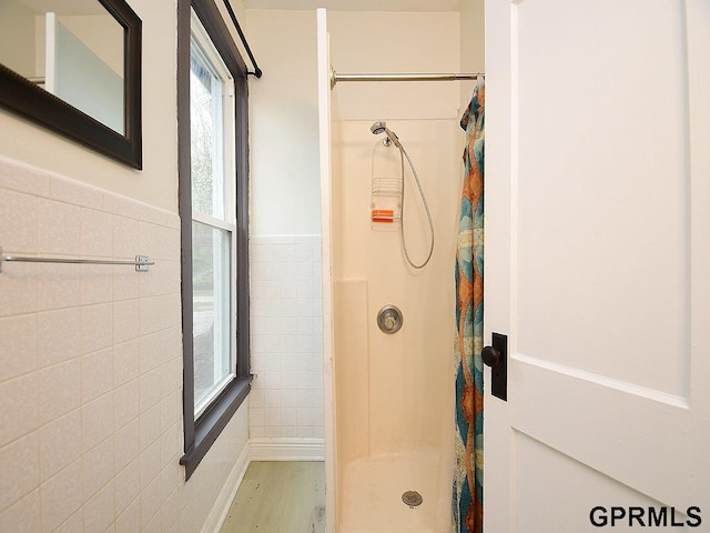 full bathroom featuring tile walls, a shower stall, wainscoting, and wood finished floors