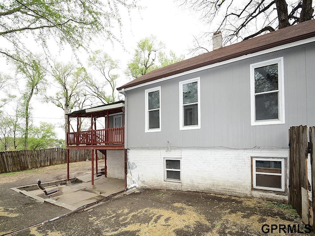 rear view of house with fence, a chimney, a wooden deck, and a patio area