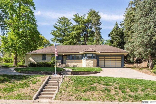 view of front of home with a garage, stone siding, concrete driveway, stairs, and a front yard