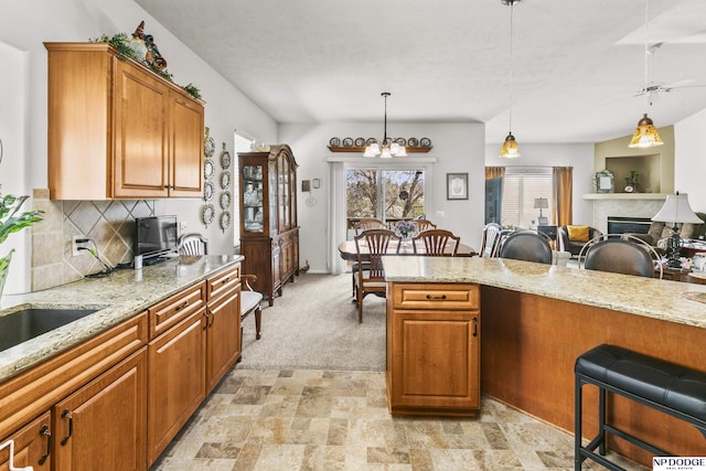 kitchen with brown cabinetry, decorative light fixtures, light stone counters, and decorative backsplash