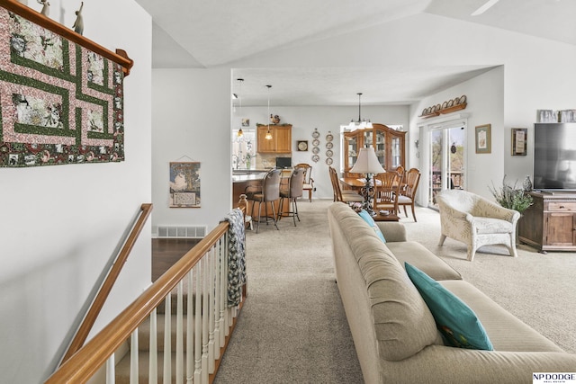 living area with an inviting chandelier, vaulted ceiling, light colored carpet, and visible vents