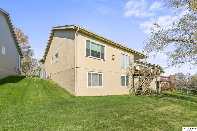 back of property with stairs, a wooden deck, central air condition unit, a yard, and brick siding
