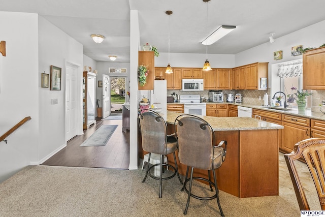 kitchen with tasteful backsplash, white appliances, light stone counters, a breakfast bar area, and a sink