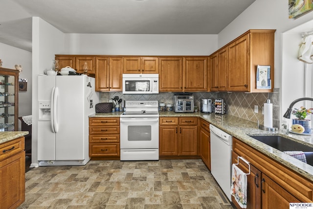 kitchen with light stone counters, stone finish floor, white appliances, and brown cabinetry