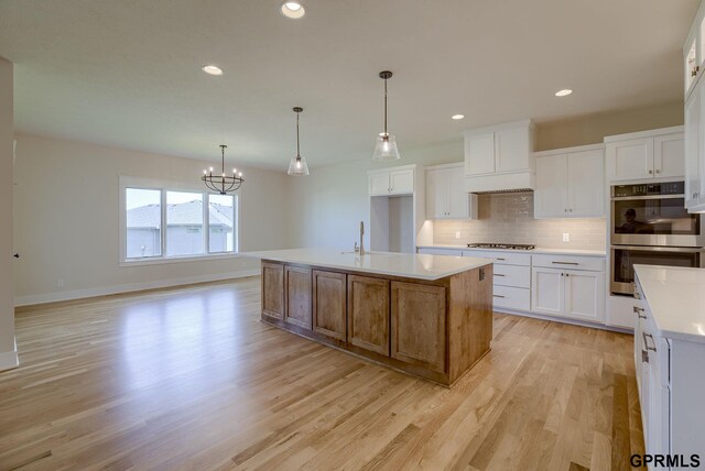 20806 Boulder St, Gretna, NE 68028 - kitchen with tasteful backsplash, white cabinets, light wood-style floors, stainless steel appliances, and a chandelier