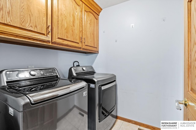 washroom featuring light tile patterned floors, separate washer and dryer, cabinet space, and baseboards
