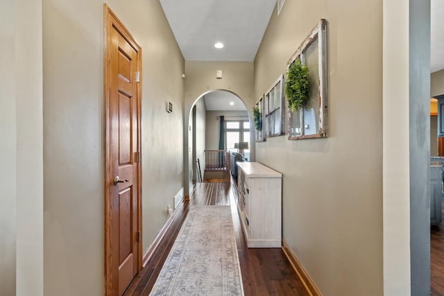 hallway with dark wood-style floors, baseboards, arched walkways, and visible vents