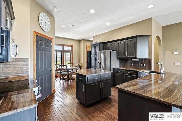 kitchen featuring arched walkways, dark stone counters, decorative backsplash, a sink, and a center island