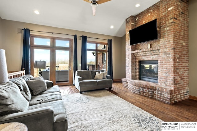 living room featuring a brick fireplace, a ceiling fan, vaulted ceiling, and wood finished floors
