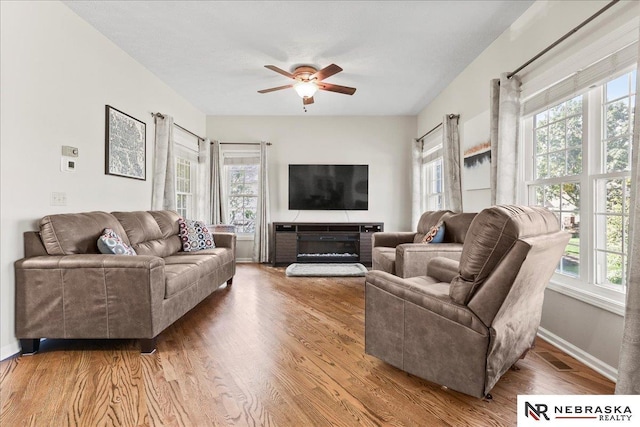 living area with baseboards, wood finished floors, and a ceiling fan