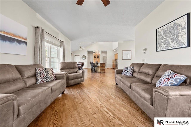 living room featuring lofted ceiling, a textured ceiling, light wood-type flooring, and a ceiling fan