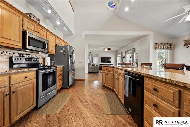 kitchen featuring stainless steel appliances, ceiling fan, open floor plan, light stone counters, and lofted ceiling