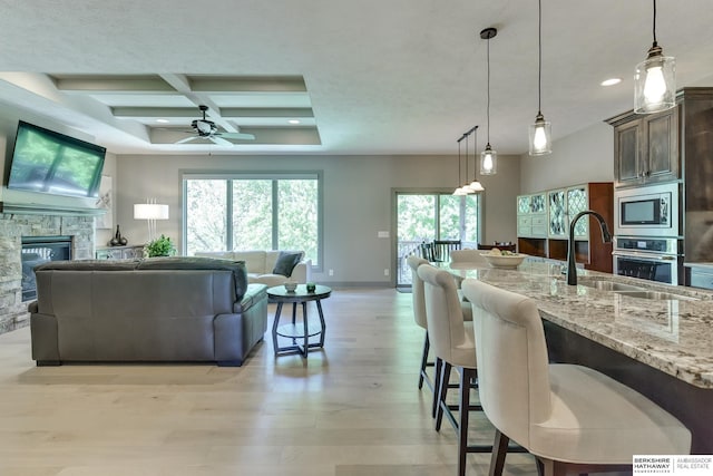 kitchen featuring open floor plan, ceiling fan, light stone counters, a sink, and appliances with stainless steel finishes