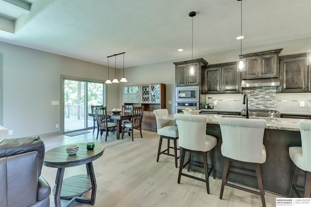 kitchen with dark brown cabinetry, tasteful backsplash, light stone counters, light wood-style floors, and stainless steel appliances
