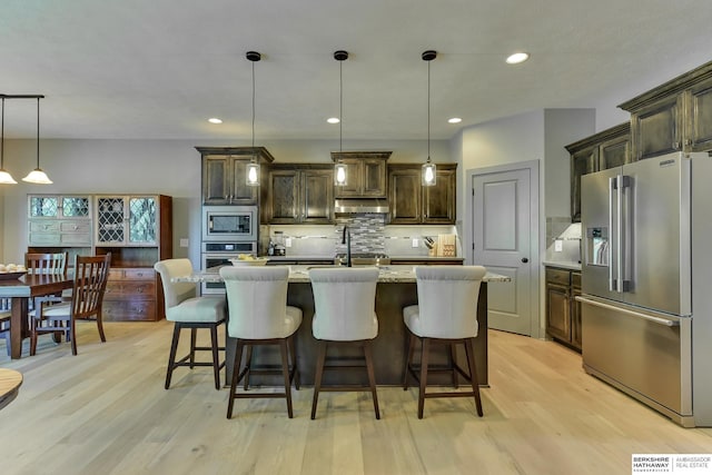kitchen featuring appliances with stainless steel finishes, light wood-style floors, decorative light fixtures, tasteful backsplash, and under cabinet range hood