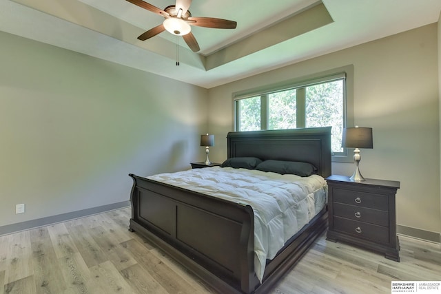 bedroom with baseboards, ceiling fan, a tray ceiling, and light wood-style flooring
