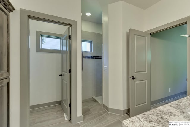bathroom featuring baseboards, a tile shower, and vanity