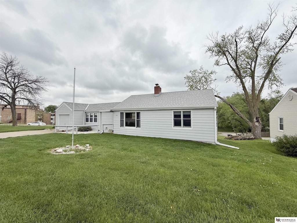 rear view of house featuring concrete driveway, a chimney, a yard, and a garage