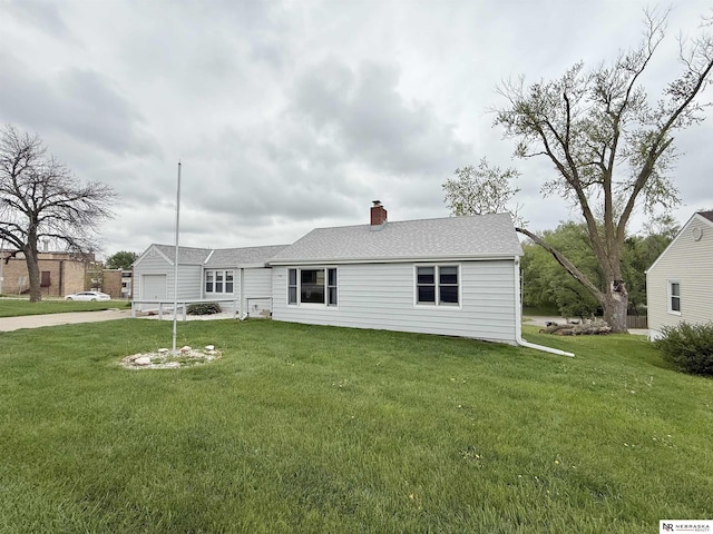 rear view of house featuring concrete driveway, a chimney, a yard, and a garage