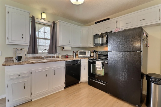 kitchen featuring white cabinetry, a sink, black appliances, a toaster, and light wood-type flooring
