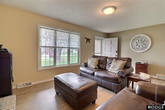 living area with baseboards, visible vents, a textured ceiling, and light wood finished floors