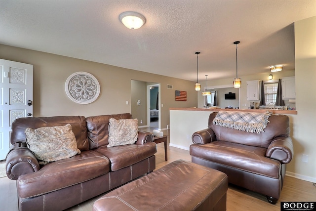 living room with a textured ceiling, baseboards, and light wood-type flooring