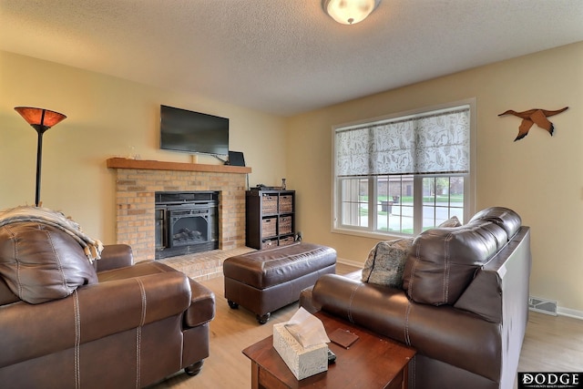 living area with light wood-type flooring, a brick fireplace, baseboards, visible vents, and a textured ceiling