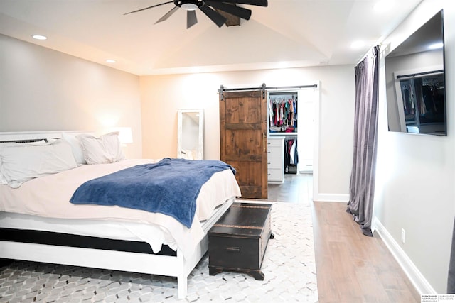 bedroom featuring a barn door, ceiling fan, recessed lighting, wood finished floors, and a walk in closet