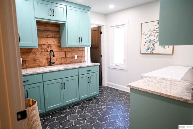 kitchen featuring light stone countertops, baseboards, recessed lighting, and a sink