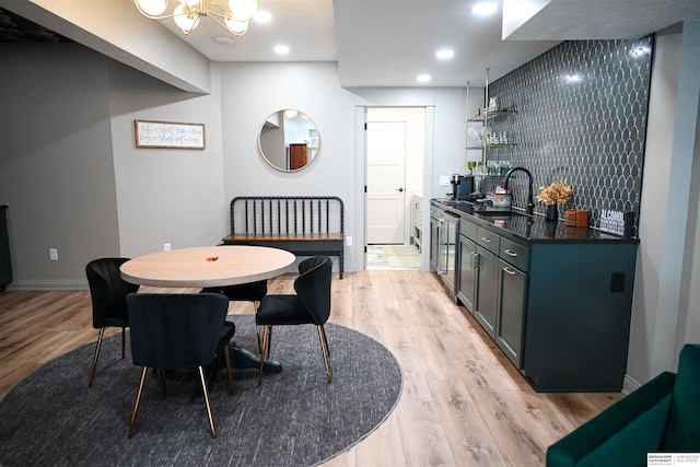 dining area with light wood finished floors, indoor wet bar, a chandelier, and baseboards